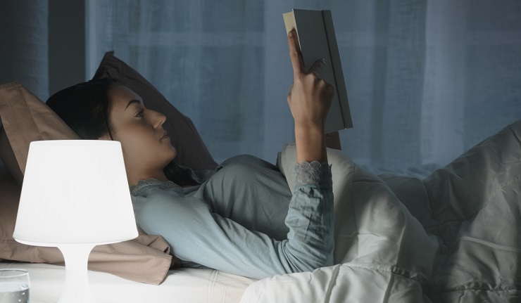 Young beautiful woman lying in bed and reading a book late at night