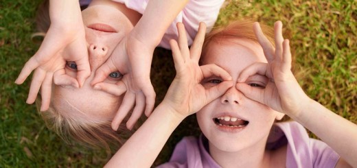 Two little girls lying on their backs making circles around their eyes with their hands
